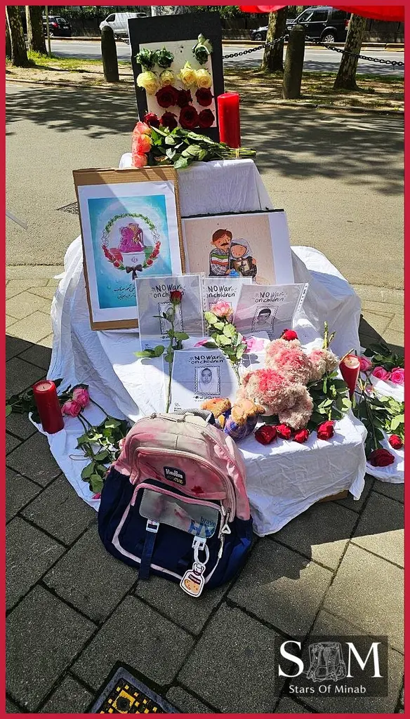 A touching display at the Brussels Minab peace gathering features a pink backpack, symbolic red candles, and a bouquet of roses, alongside framed artwork and touching messages advocating for children