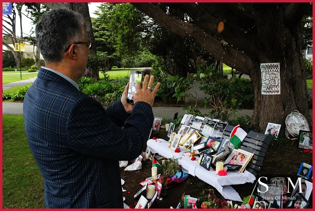 A visitor photographs a serene memorial display on campus during the San Francisco State University vigil, soft light and flowers convey quiet grief